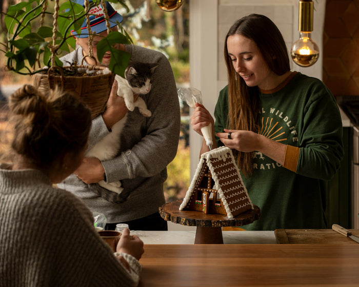 A person decorating an A-frame gingerbread house with icing